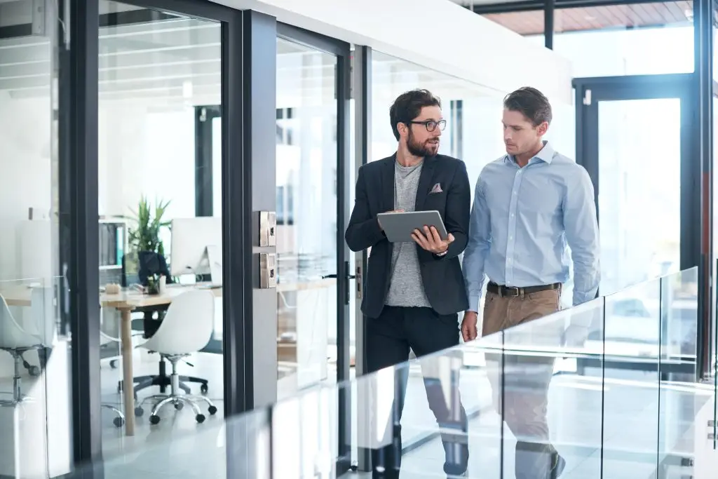 Two businessmen standing in an office looking at a tablet.