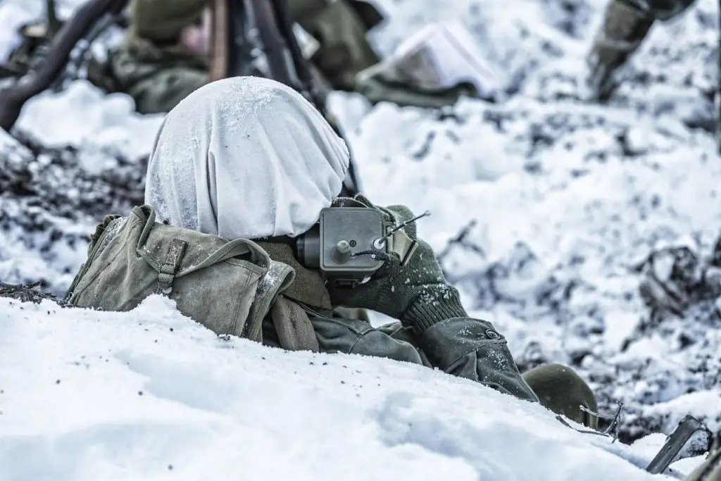 A soldier is sitting in the snow with a radio.