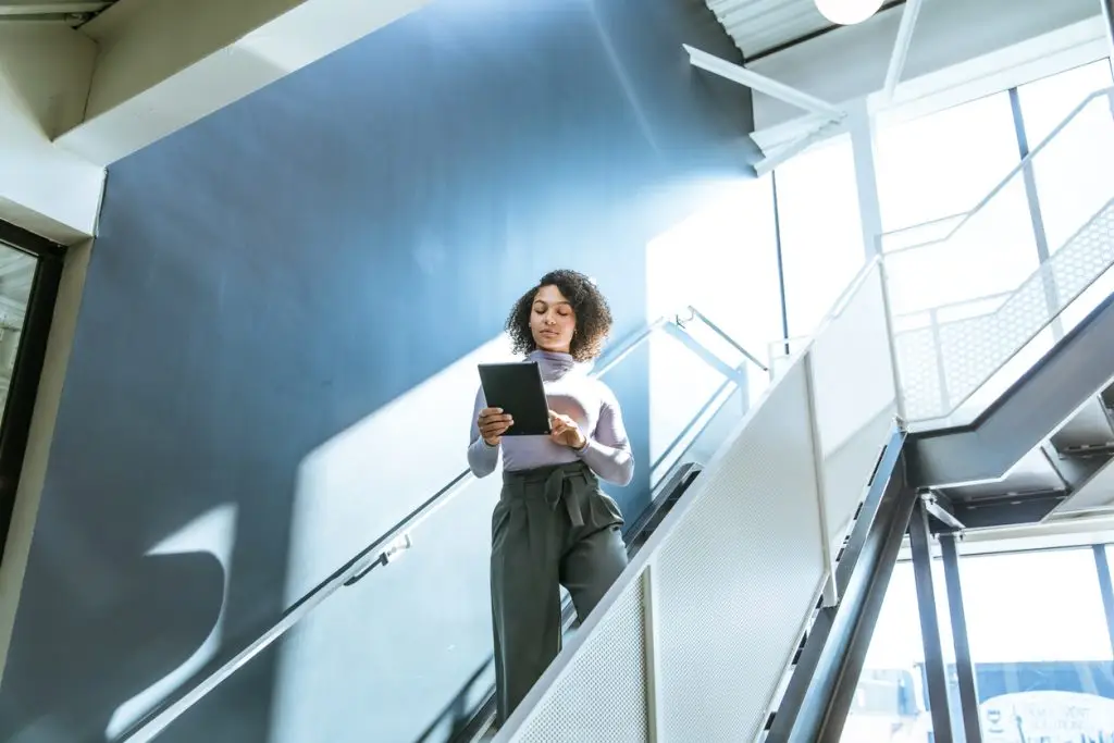 A business woman standing on an escalator holding a tablet.