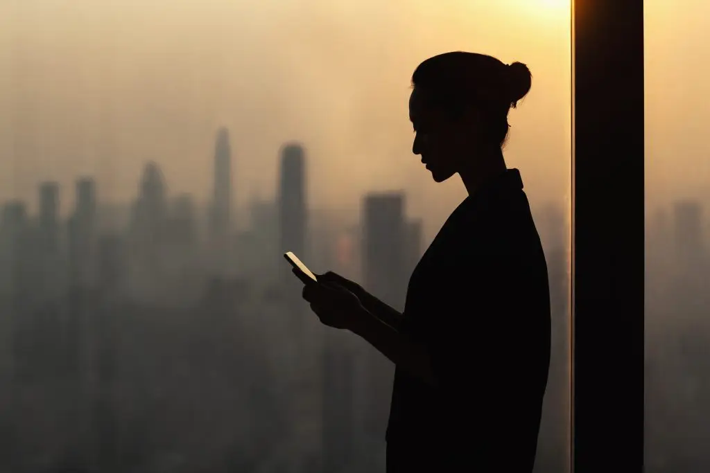 Silhouette d'une femme utilisant un téléphone portable devant une ville.