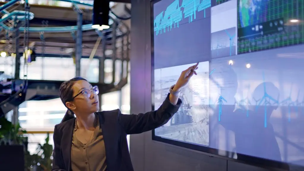 A woman is pointing at a large screen in an office.