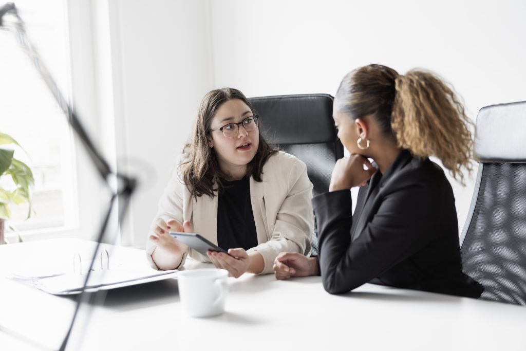 Two business women talking at a table in an office.