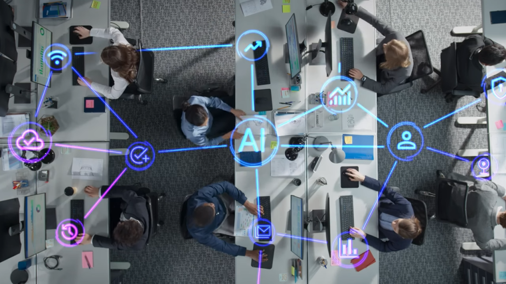 Top-down view of a workspace with people at desks interacting with computers. Overlayed graphics and icons denote AI and connectivity concepts.