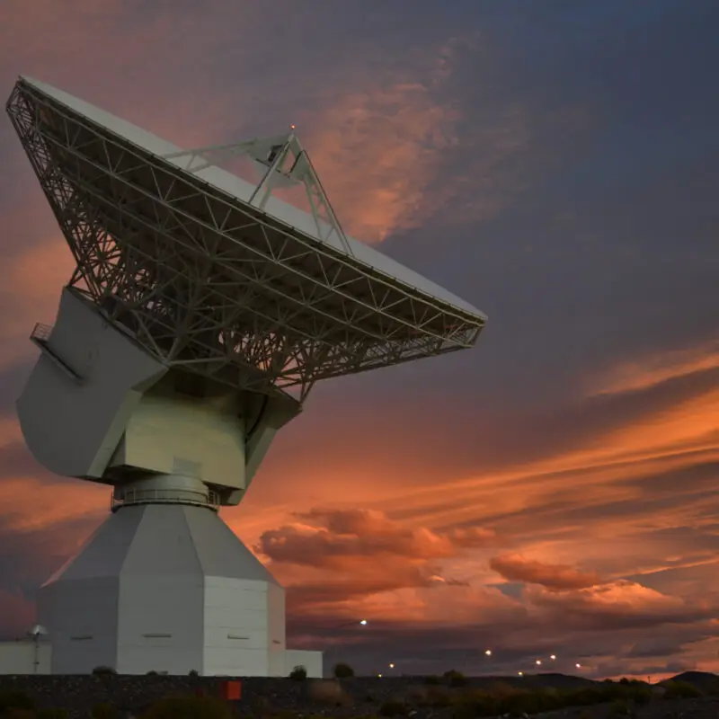 A deep space antenna pointed at the sky, as the sun sets on the horizon.