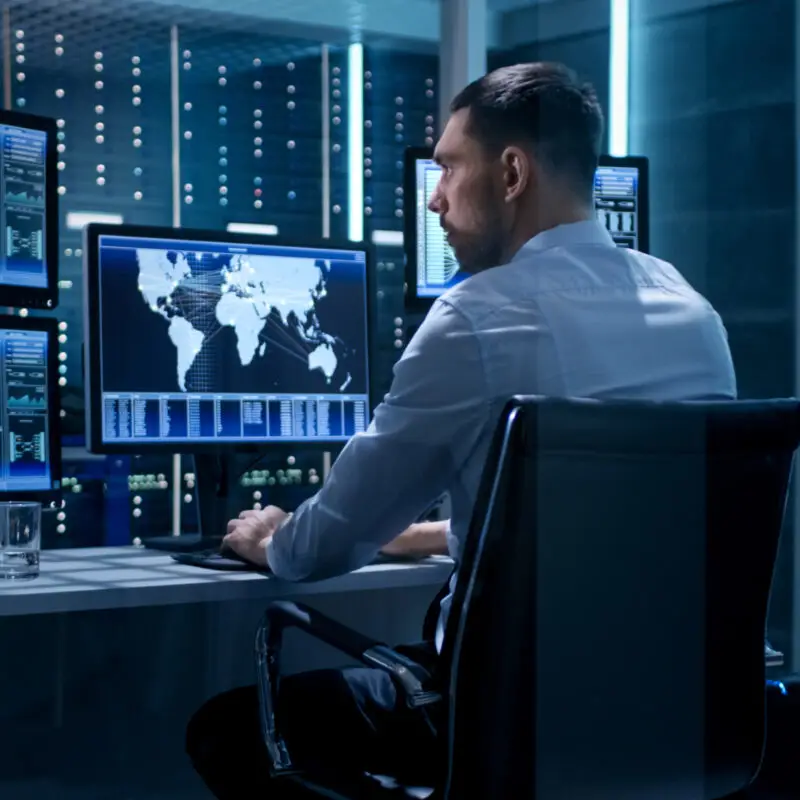 Un homme assis à un bureau, devant un ordinateur qui affiche une carte du monde illuminée.