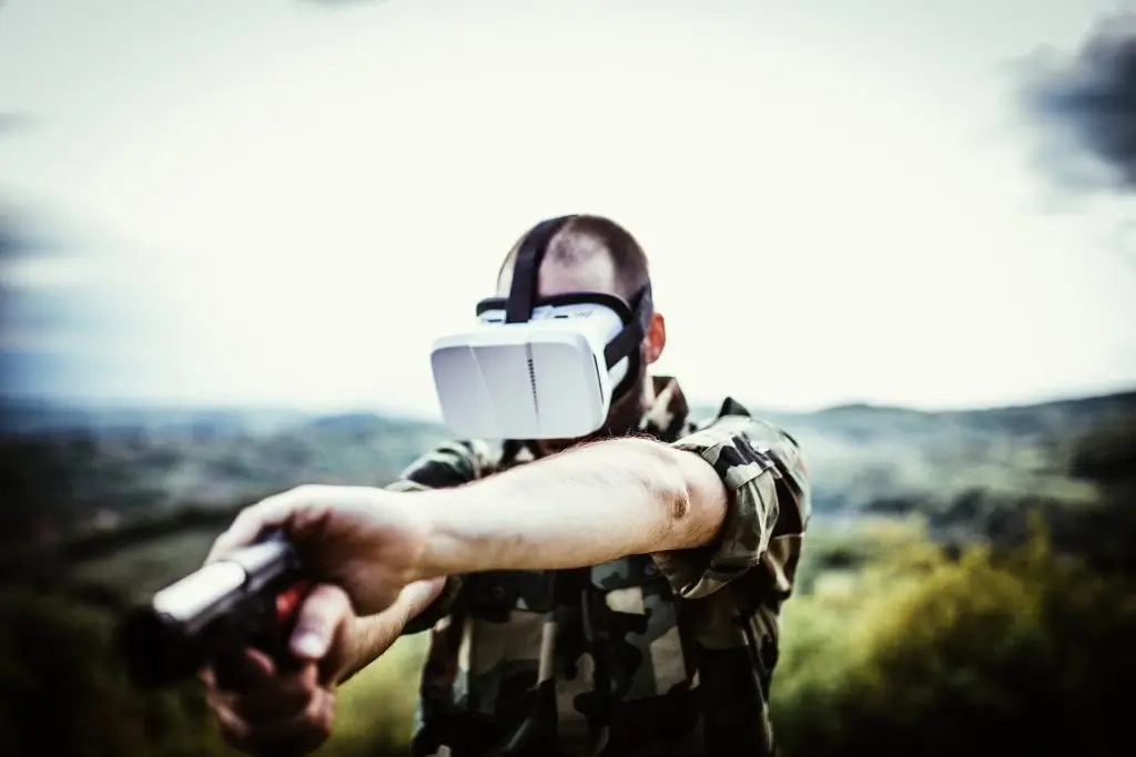 Soldat dans la montagne guettant avec une arme à la main, il porte un casque de réalité virtuelle