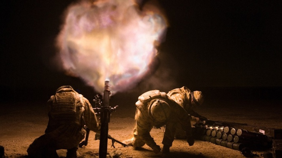 Two soldiers operate a mortar at night, with one loading shells and the other firing, creating a bright burst of light.