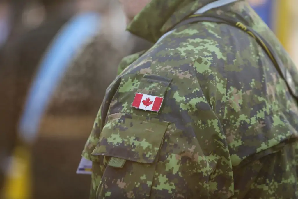 A person wearing a Canadian military camouflage uniform with a Canadian flag patch on the sleeve.