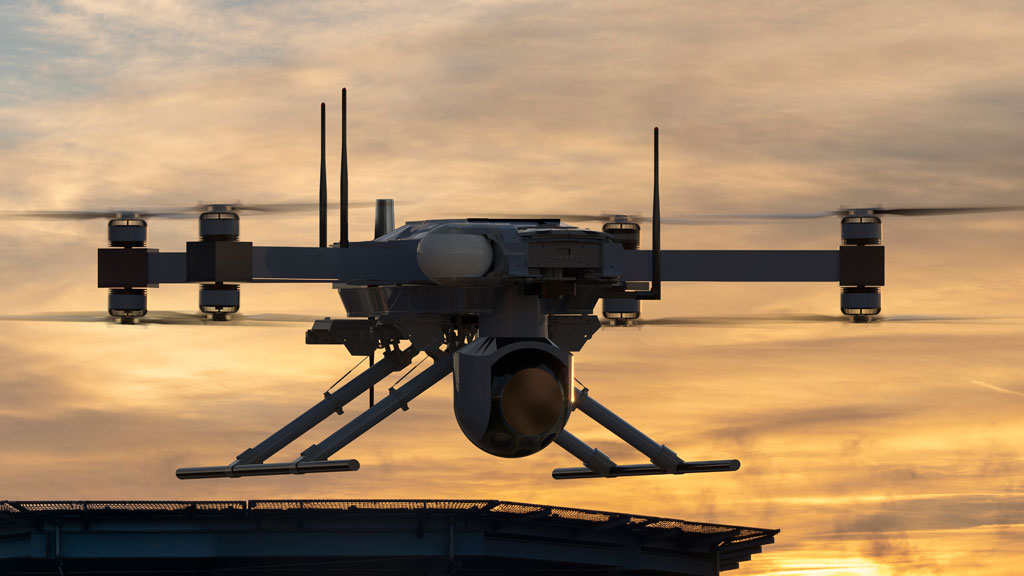 A quadcopter drone with a mounted camera hovers above a rooftop at sunset, silhouetted against the sky.