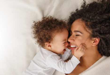 A woman kissing her baby while lying on a bed.