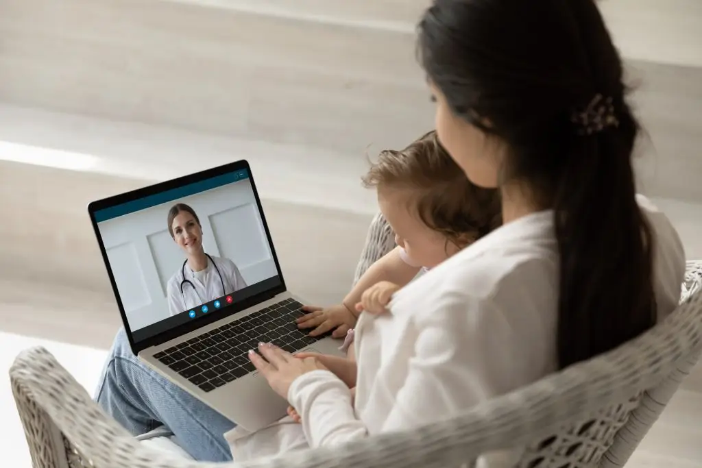 A woman and her child are using a laptop to video chat with a doctor.