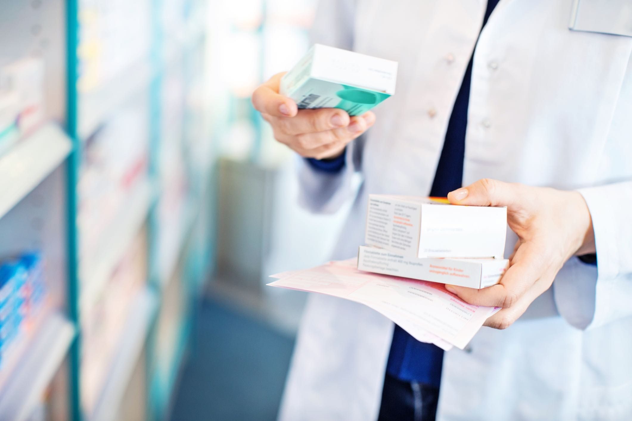 A pharmacist is holding a box of medicine in a pharmacy.