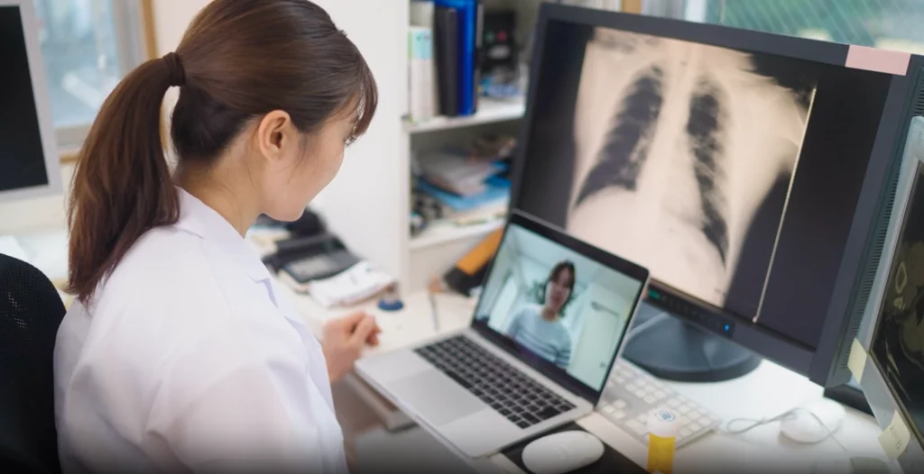 A woman in a white coat is looking at an x - ray image on a laptop.