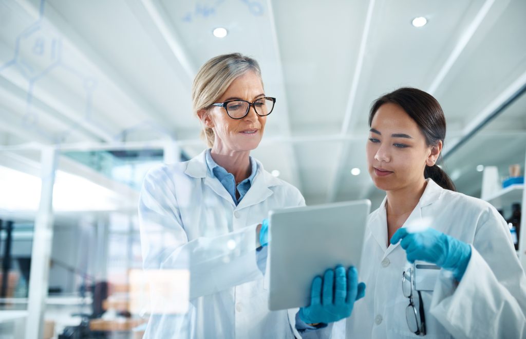 Deux scientifiques en blouse et gants examinent l'écran d'une tablette dans un laboratoire moderne.