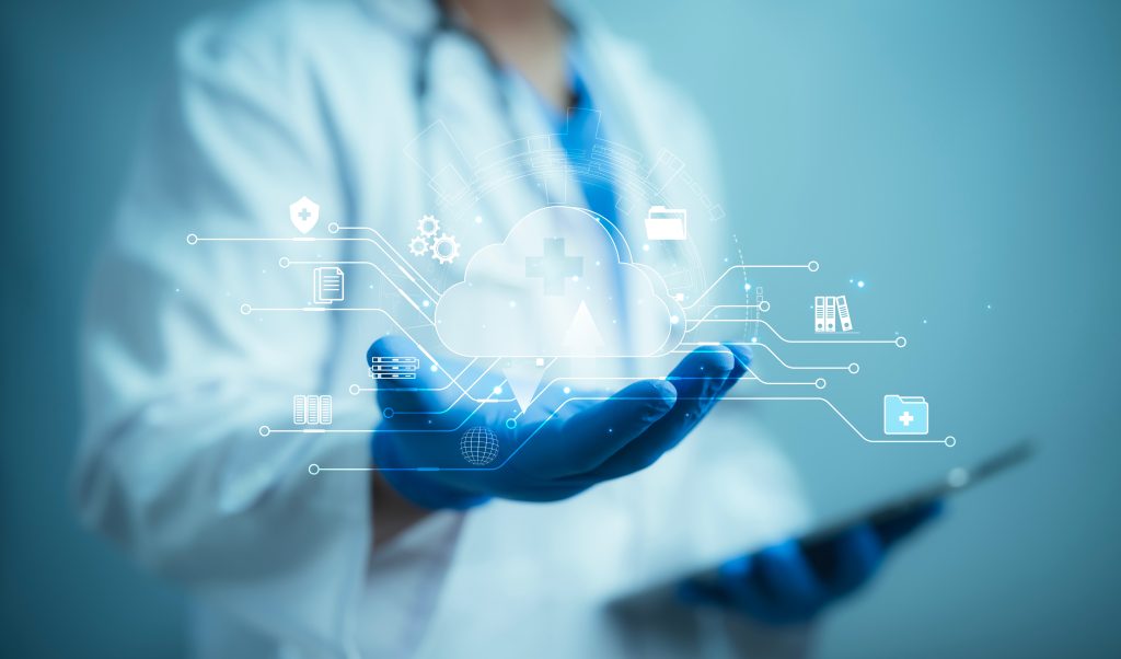 Doctor in a lab coat and gloves holding a tablet. Digital cloud graphics with medical icons hover above the doctor's hand, symbolizing healthcare technology.