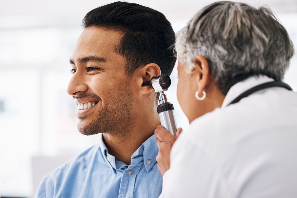 A healthcare professional examines a smiling man's ear with an otoscope during a medical checkup.