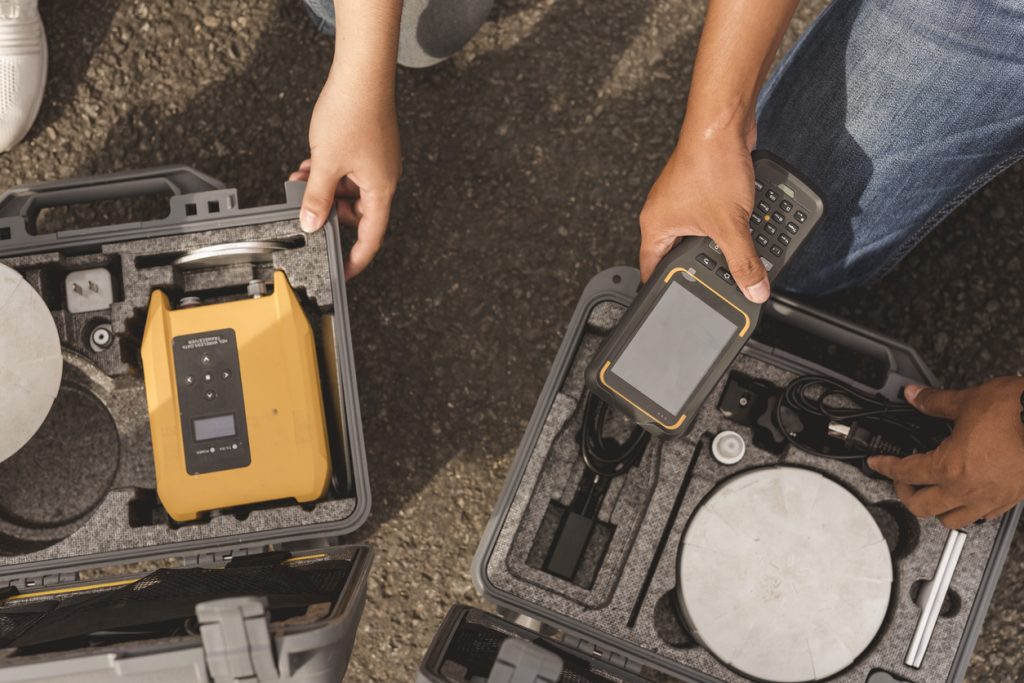 Surveryors setting up real-time kinematic or RTK geodetic surveying equipment used in the field. A GNSS receiver, GPS rugged field controller and transceiver.