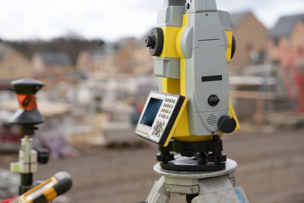 Surveyor builder site engineer with theodolite total station at construction site outdoors during surveying work