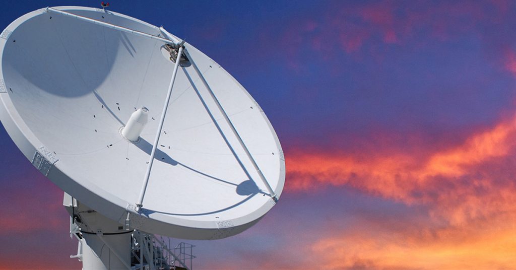 A large satellite dish pointing upward against a vibrant sunset sky with hues of blue and orange.