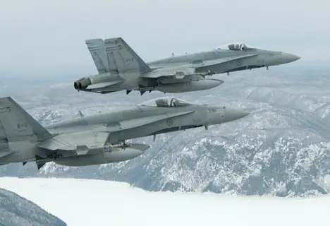 Two military jets flying in formation over a snowy mountainous landscape.