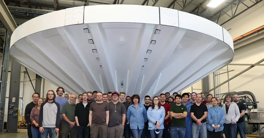 A group of employees standing in front of a large, circular industrial structure in a warehouse.