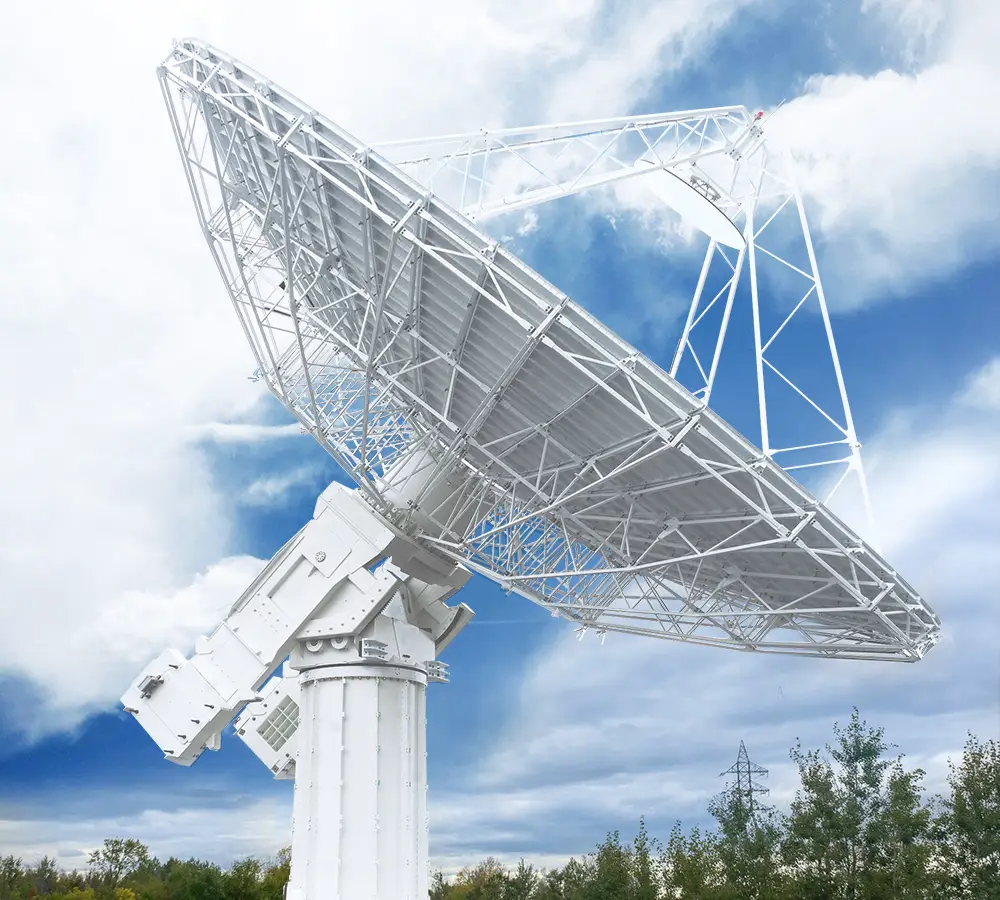 Grande antenne blanche de radiotélescope pointant vers le haut dans un ciel partiellement nuageux avec des arbres en arrière-plan.