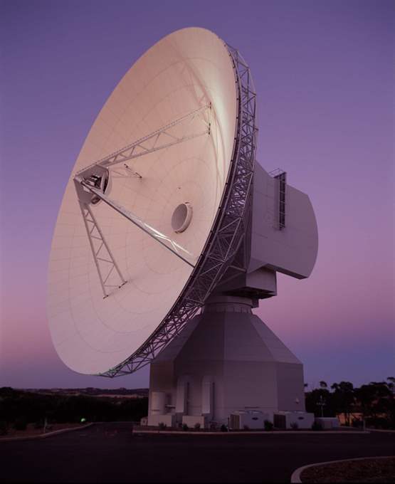 A large satellite dish antenna against a dusky pink sky, angled upwards to receive signals.