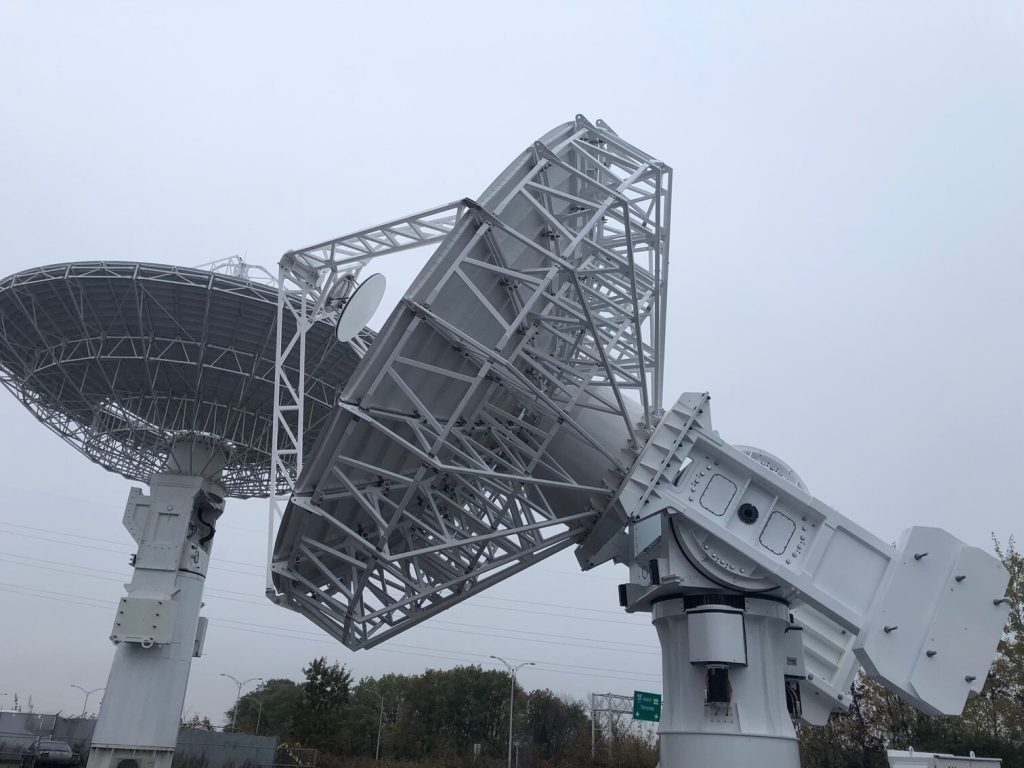 Two large, white satellite dishes on metal supports, focused upwards, against an overcast sky.