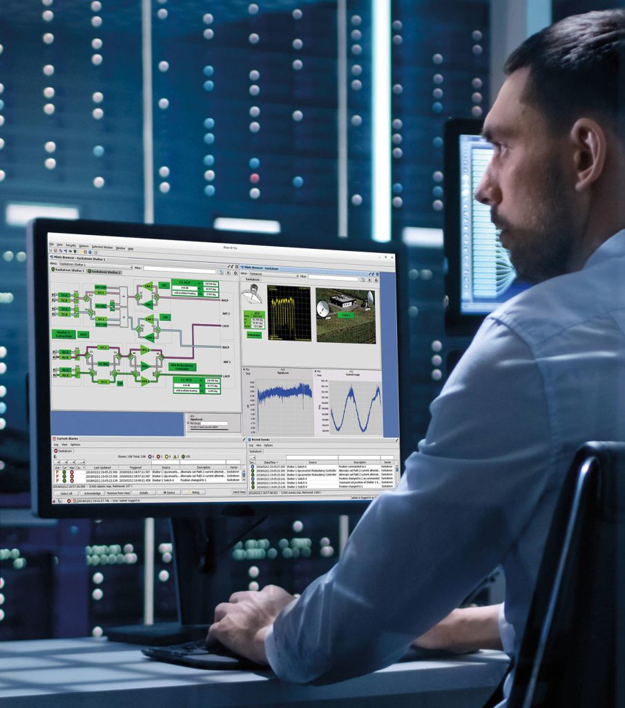 A man is working on a computer with a complex data analysis program displayed on the screen. He is seated in a high-tech environment, possibly a data center or control room.