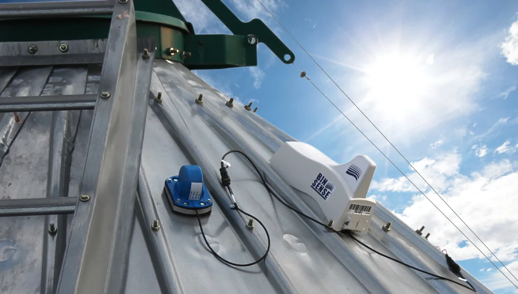 A metal roof with an antenna and sensor devices mounted under a sunny sky, with a ladder attached to the roof.