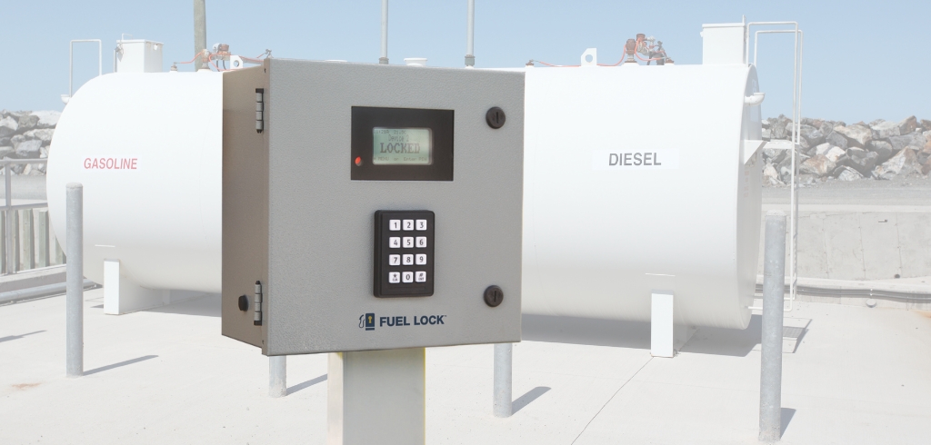 A fuel lock control panel with a keypad and display is mounted on a post in front of two large fuel storage tanks labeled "Gasoline" and "Diesel.