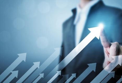 Businessman pointing at a rising arrow graphic, symbolizing growth or success, with a blurred background.