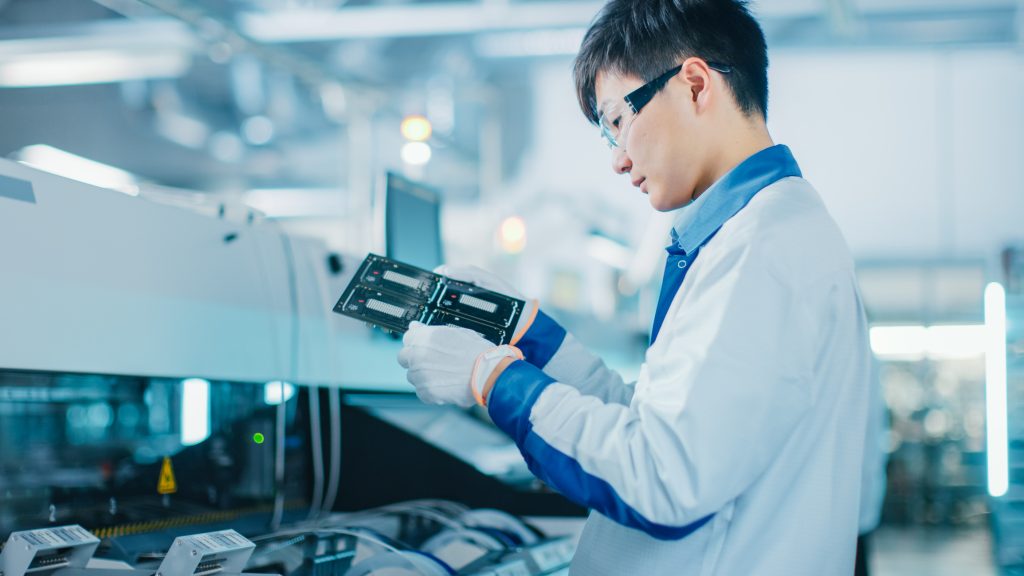 Asian male engineer inspecting a computer part in a high-tech manufacturing facility.