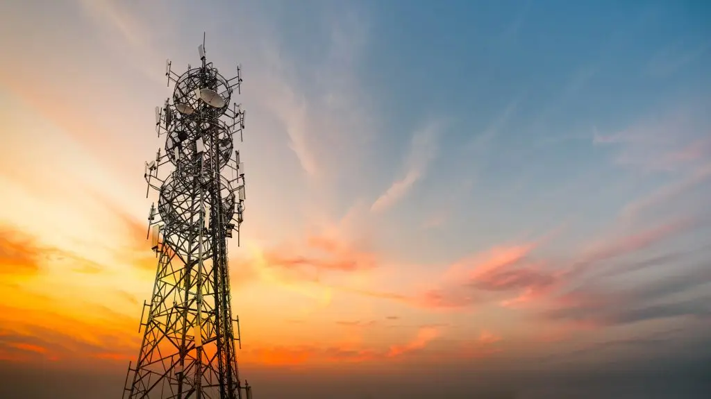 A telecommunications tower stands against a vibrant sunset sky, equipped with numerous antennas for broadcasting and communication purposes.