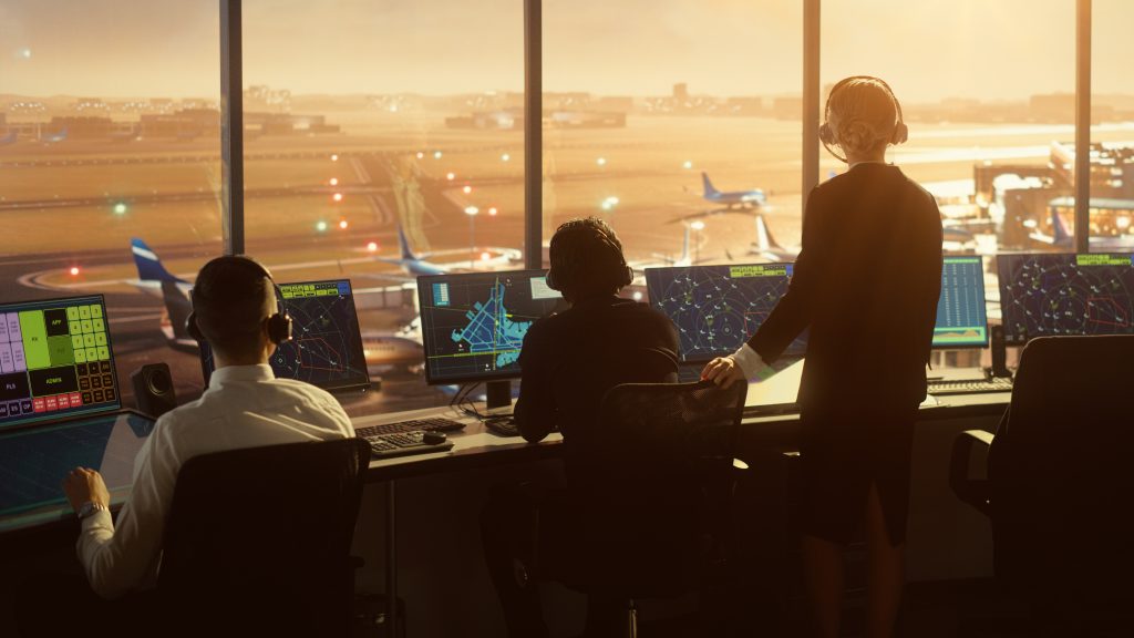 Air traffic controllers monitoring and coordinating flights from a control tower with computers and radar screens, overlooking an airport runway at sunset.