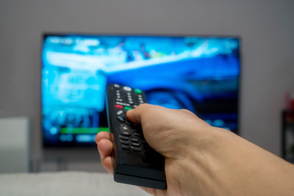 A person points a remote control at a television displaying a blue-toned image.