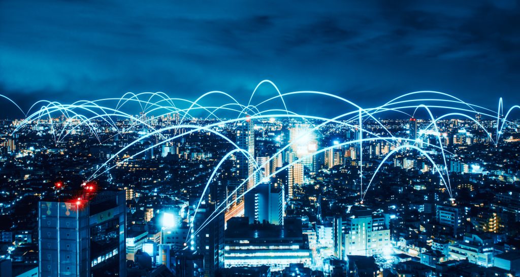 A nighttime cityscape with illuminated buildings and light trails forming arcs in the sky, depicting the concept of data transfer.