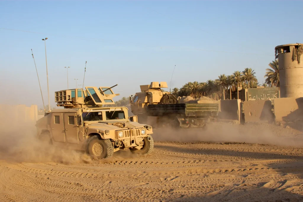 A humvee and a tank in a dusty road maneuver during a military exercise in a desert setting.
