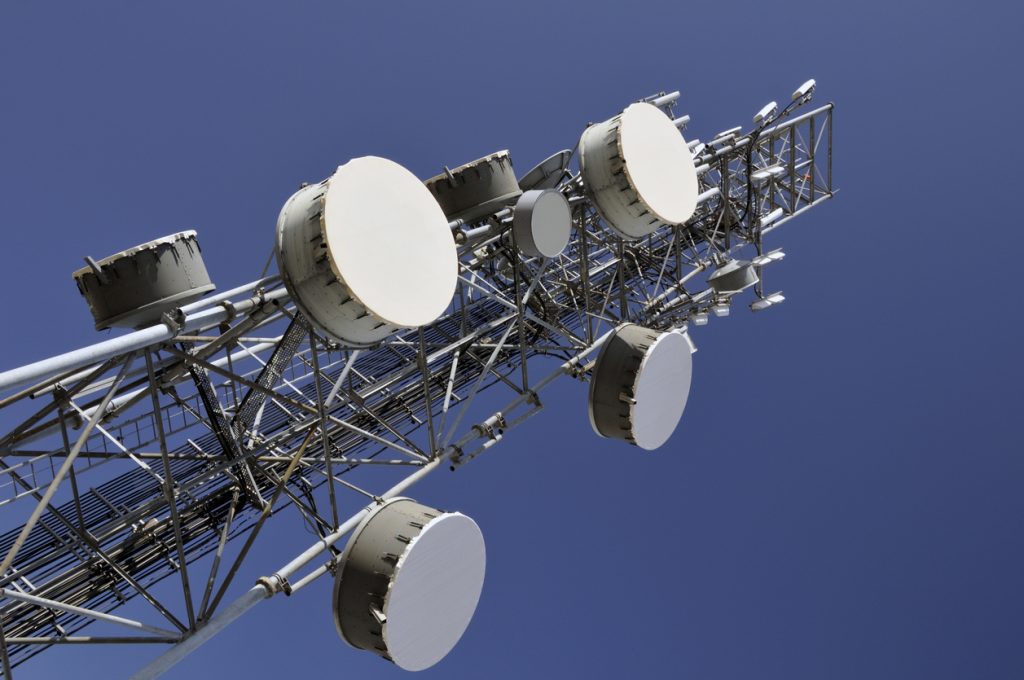 A telecommunications tower with multiple large circular antennas attached, against a clear blue sky.