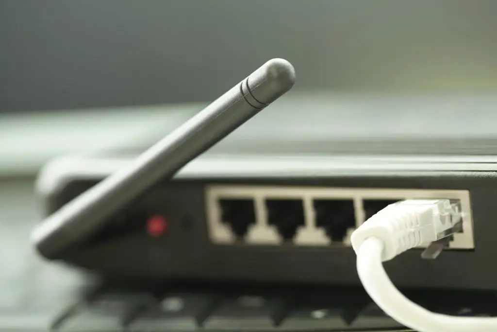 Gros plan d'un routeur noir avec antenne, montrant quatre ports Ethernet à l'arrière, dont l'un est connecté via un câble Ethernet blanc.