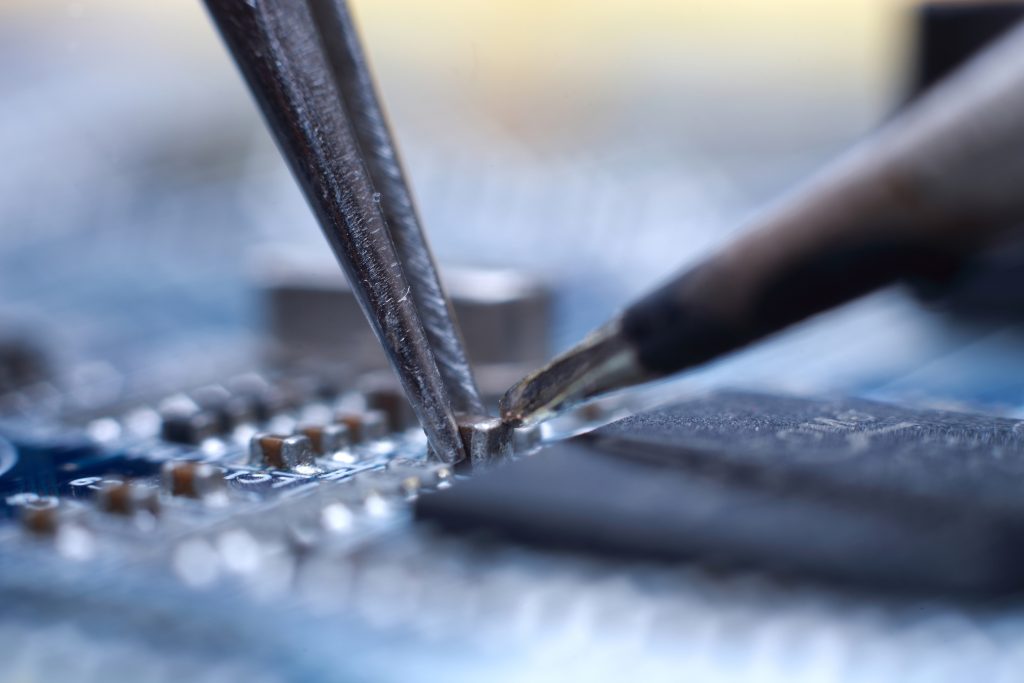 Close-up of a soldering iron being used on a circuit board component, highlighting precise electronic repair work.