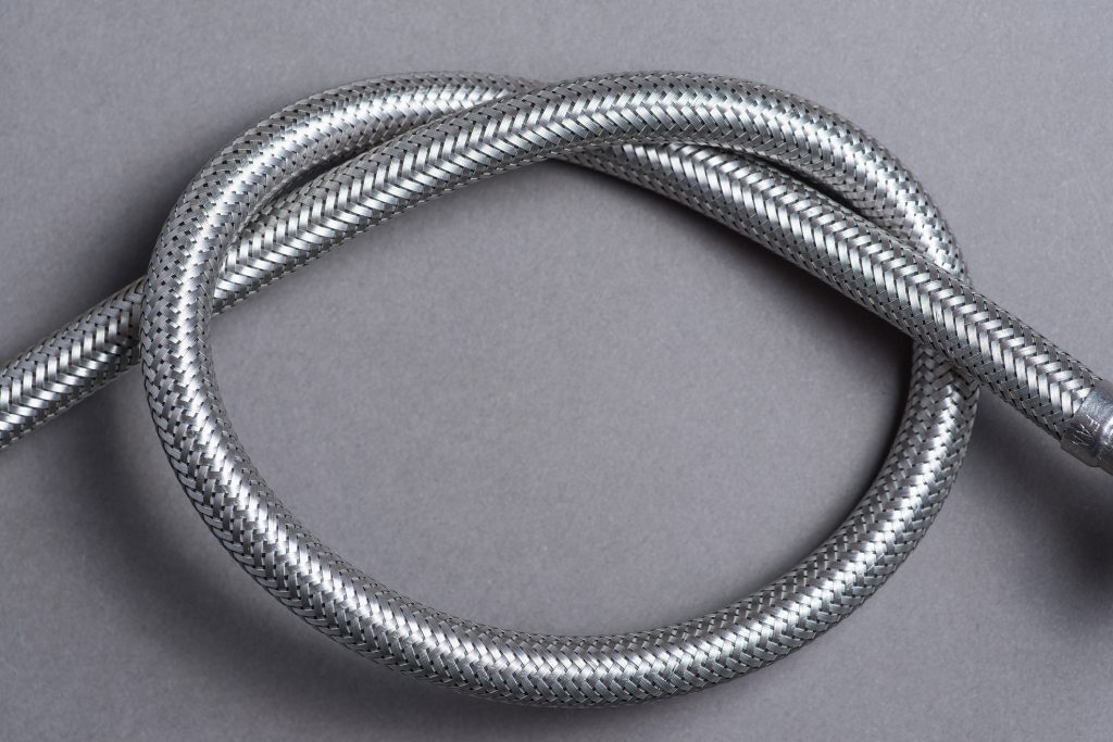 Close-up of a coiled, silver, metal braided hose on a grey background.
