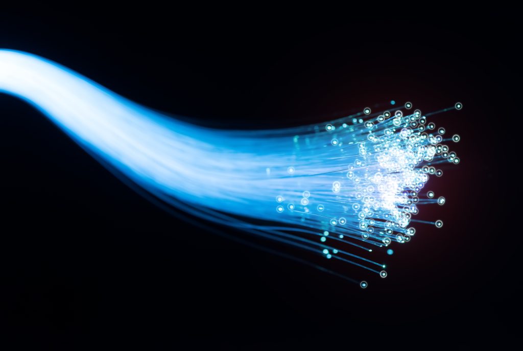 Image en gros plan d'un câble de fibre optique émettant un flux de lumière bleue sur un fond sombre, représentant une transmission de données à grande vitesse.