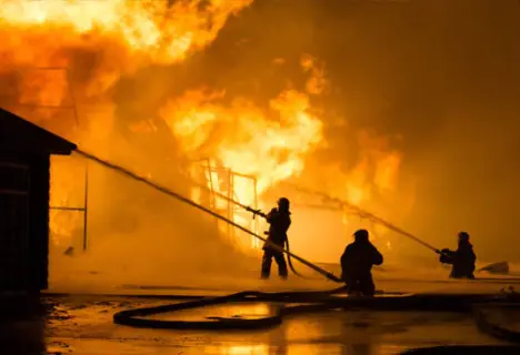 Firefighters using hoses to battle a large blaze engulfing a building at night.