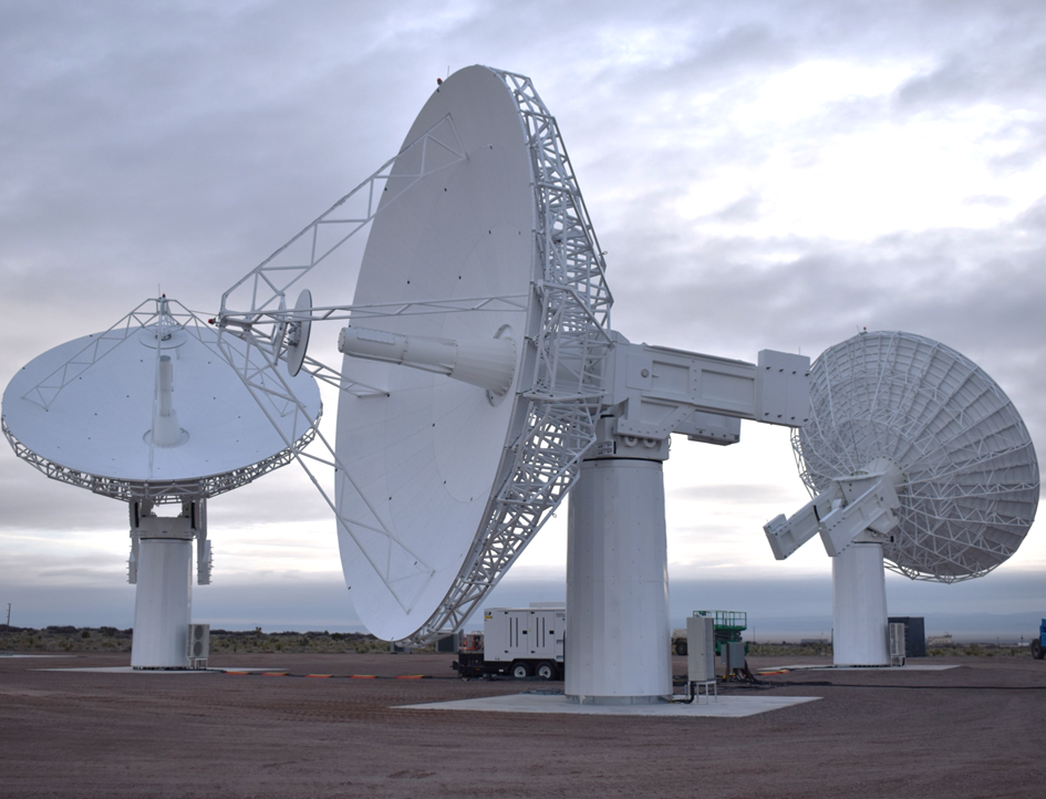 Three large white radio telescopes on a flat landscape under a cloudy sky.