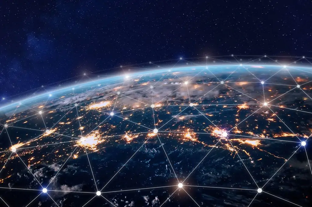 Vue de la Terre depuis l'espace, de nuit, montrant des villes illuminées reliées par un réseau de lignes blanches et de nœuds lumineux, symbolisant la connectivité numérique mondiale.