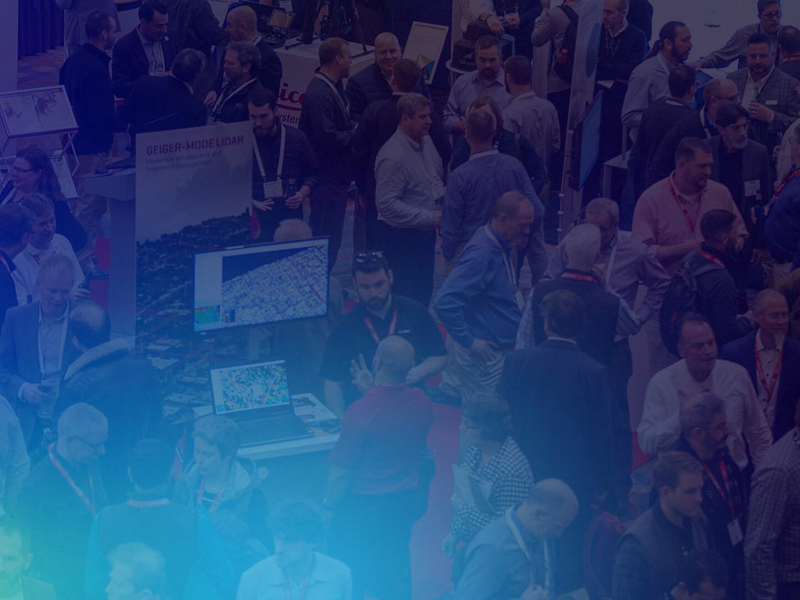 A crowded exhibition hall with people interacting around booths and displays featuring computer screens and informational posters.