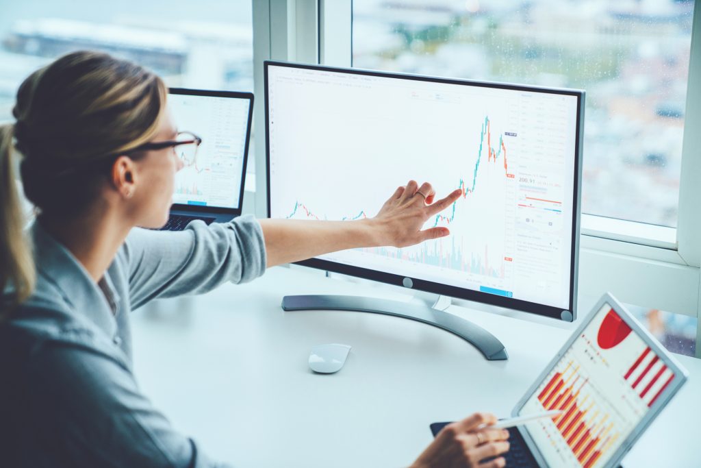 Un professionnel analysant des données financières sur deux écrans d'ordinateur avec des graphiques et des tableaux.