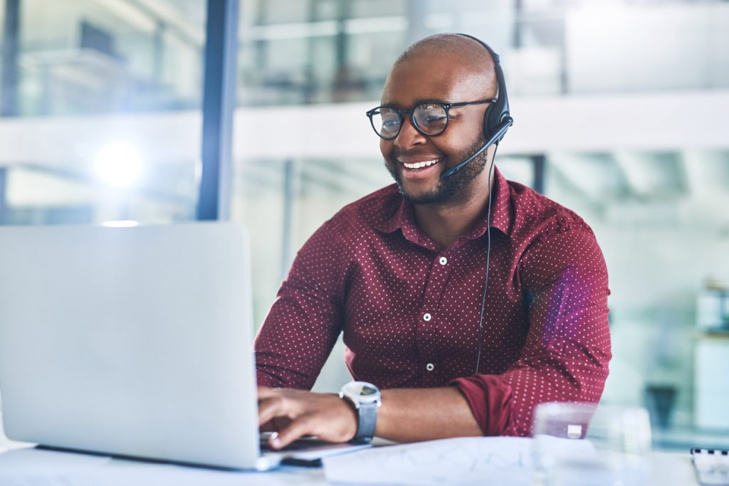 Un homme souriant portant un casque et travaillant sur un ordinateur portable dans un bureau.