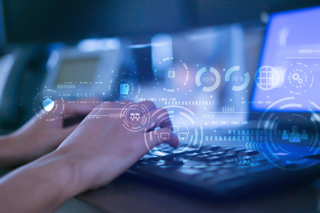 A person typing on a laptop with a computer screen.